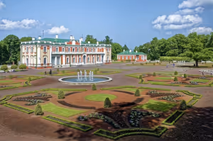 Rot-weißes Barockschloss mit Springbrunnen und formalem, gemustertem Blumengarten unter blauem Sommerhimmel