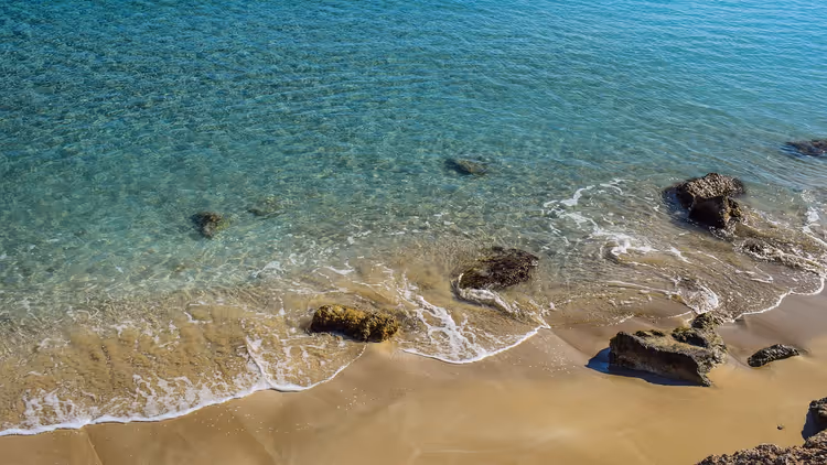 Sandstrand mit flachem, klarem Wasser und Felsen
