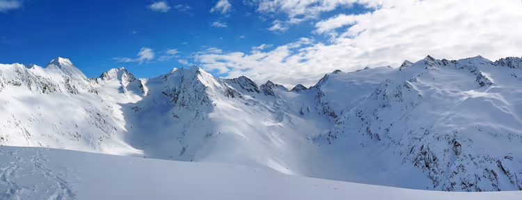 Schneebedeckte Alpengipfel und unberührte Hänge unter blauem Himmel mit vereinzelten Wolken in Österreich