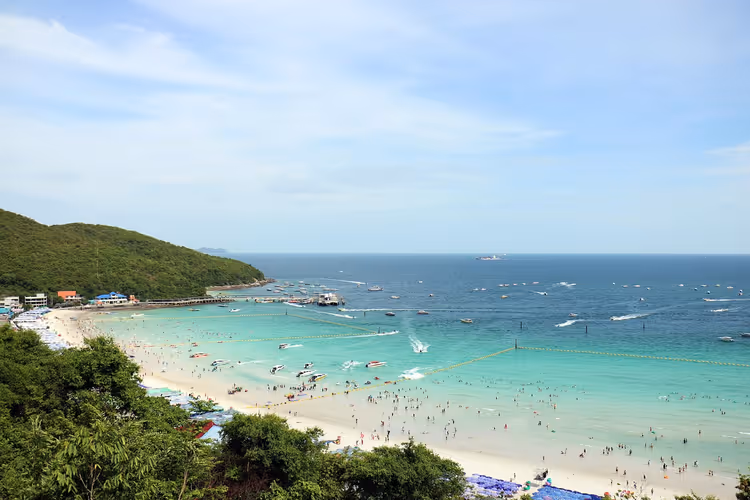 Voller weißer Sandstrand und türkisfarbene Bucht mit vielen Schnellbooten bei Pattaya, Blick von einem grünen Hang