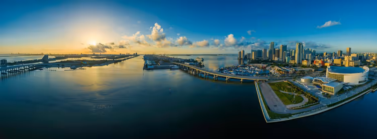 Luftpanorama einer Bucht bei Sonnenuntergang mit Brücken, einem Jachthafen und einer Hochhaus-Skyline rechts