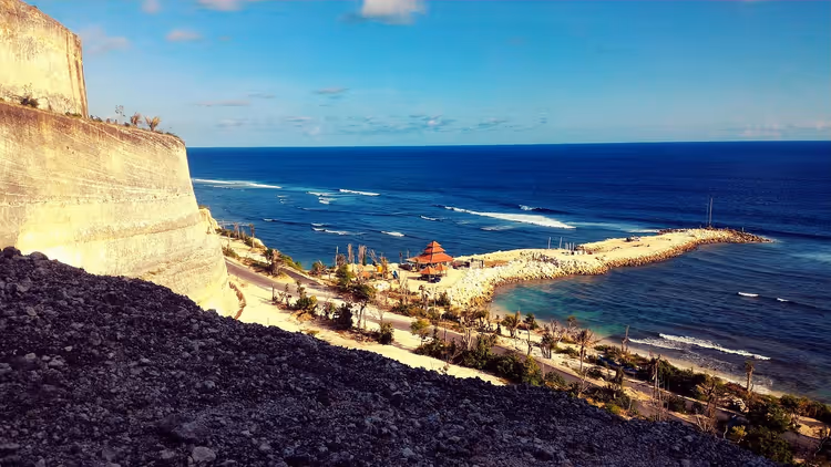 Rotsachtige kust met een pier en een tempel op Bali