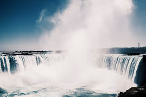 Horseshoe Falls an den Niagarafällen, eine hohe weiße Gischtwolke steigt vom geschwungenen Wasservorhang in den blauen Himmel