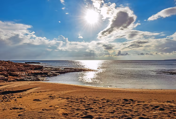Zandstrand, zee, rotsen en zon