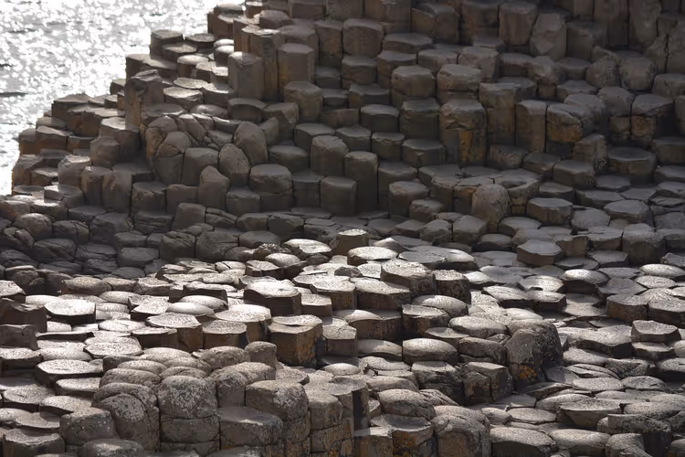 Sechseckige Basaltsäulen des Giant's Causeway, die als gestufte Steinterrassen zum glitzernden Meer hinabführen