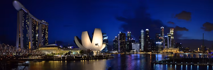 Skyline von Singapur bei Nacht mit Marina Bay Sands, dem lotusförmigen Museum und beleuchteten Wolkenkratzern, gespiegelt in der Bucht