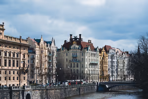 Palazzi Art Nouveau riccamente decorati lungo un argine in pietra vicino a un ponte a Praga sotto un cielo nuvoloso