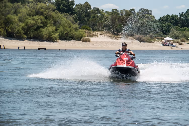Mann på vannscooter i høy fart gjennom sjøvann langs kysten