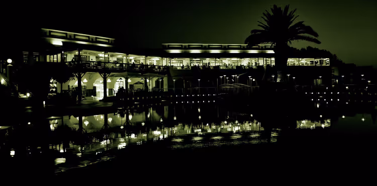 Hotel bij nacht met zwembad, weerspiegelingen en een palmboom
