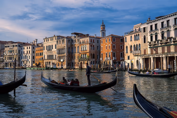 Gondoliere rudert Fahrgäste über den Canal Grande in Venedig, vorbei an farbigen Palazzi unter dem Abendhimmel