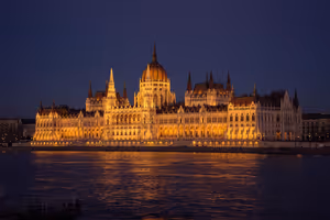 Ungarisches Parlament in Budapest bei Nacht golden beleuchtet, Kuppel und Türme spiegeln sich in der Donau