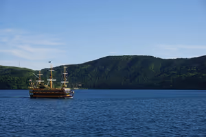 Utflyktsfartyg i piratstil korsar Ashisjöns blå vatten i Hakone, med skogklädda kullar bakom