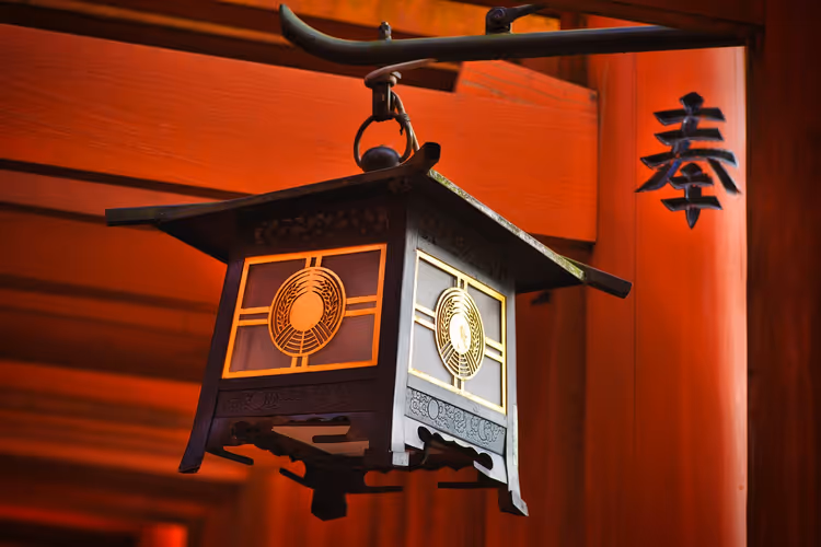 Dunkle Metalllaterne mit goldenem Ornament, die an einem zinnoberroten Torii an einem Schrein in Japan hängt