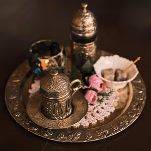 Graviertes Metalltablett mit türkischer Kaffeetasse samt Deckel, Lokum in einer weißen Schale, rosa Rosen und einer Kerze