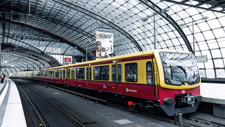 Rot-gelbe S-Bahn steht unter dem gewölbten Glasdach eines Berliner Bahnhofs