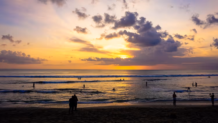 Sonnenuntergang über dem Meer, Menschen am Strand und im Wasser
