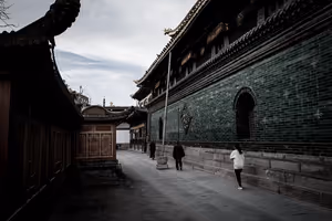 Ruhige Gasse in China zwischen einer Tempelmauer aus grünen Ziegeln und Holzhallen mit geschwungenen Dächern, einige Menschen unterwegs