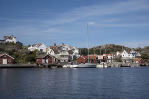 Rote Bootshäuser und weiße Holzhäuser an einem felsigen Ufer mit vertäuten Segelbooten in einem schwedischen Küstendorf
