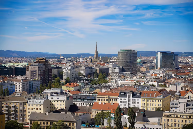 Dächer von Wien von oben mit dem Turm des Stephansdoms und modernen Hochhäusern unter blauem Himmel