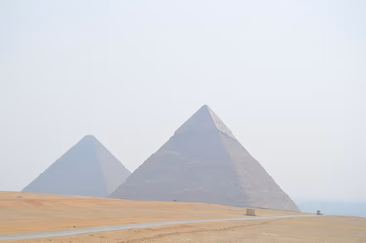 To av pyramidene i Giza som reiser seg gjennom blek ørkendis over et sandplatå og en tom vei i Egypt