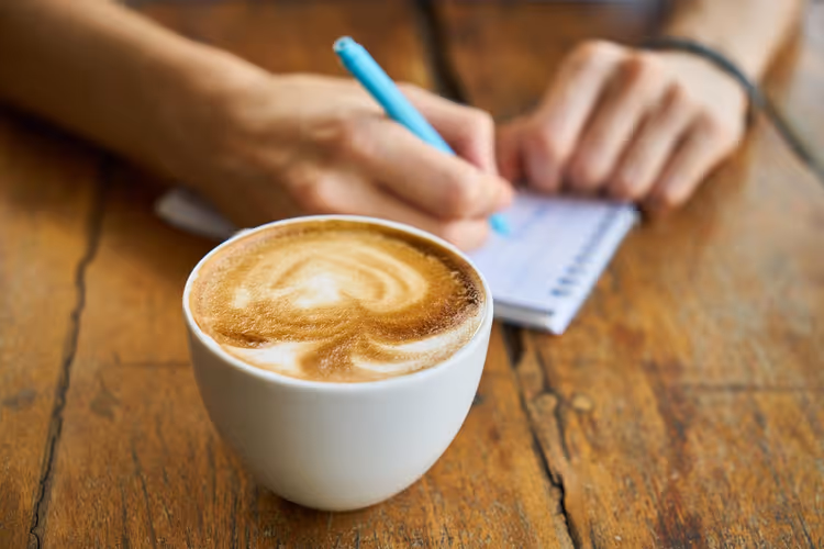 Cappuccino en handen met een notitieboekje aan het werk in een café