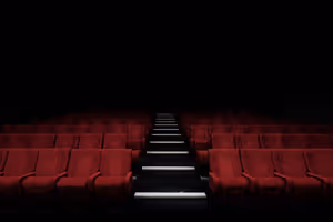 Reihen leerer roter Samtsitze zu beiden Seiten eines beleuchteten Stufengangs in einem dunklen Theatersaal