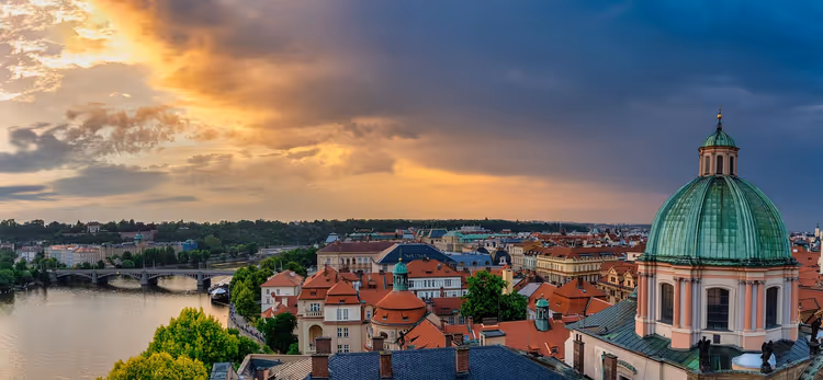 Grüne Kupferkuppel und rote Dächer der Prager Altstadt an der Moldau unter einem dramatischen Abendhimmel