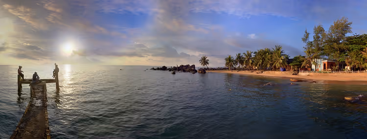 Tropischer Strand mit Pier und Palmen bei Sonnenuntergang