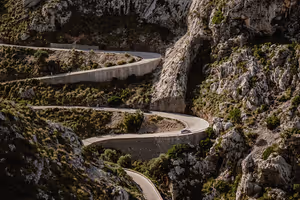 Schmale Straße schlängelt sich in Haarnadelkurven einen steilen, felsigen Berghang mit spärlichem grünem Gestrüpp auf Mallorca hinab