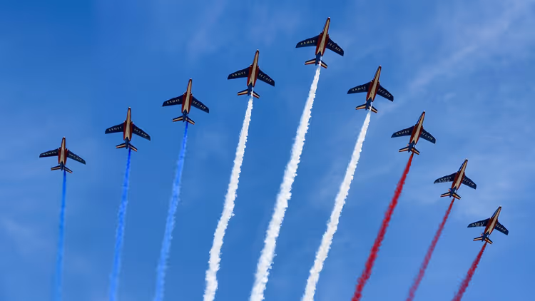 Neun Militärjets im Formationsflug mit blauen, weißen und roten Rauchspuren vor blauem Himmel, Frankreich