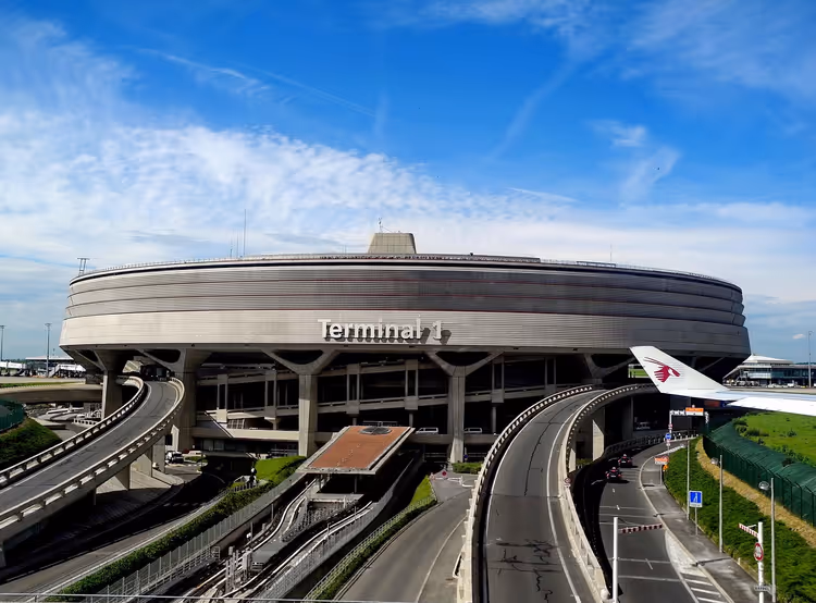 Rundes Betongebäude des Terminals 1 am Flughafen Paris Charles de Gaulle mit geschwungenen Zufahrtsrampen unter blauem Himmel