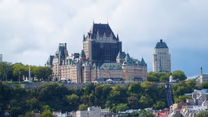 Château Frontenac mit Kupferdächern und Türmchen auf einer bewaldeten Klippe über der Unterstadt von Québec