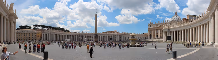 Panorama eines weiten Platzes mit Kolonnaden im Vatikan mit Obelisk in der Mitte, Kuppel der Basilika und vielen Besuchern
