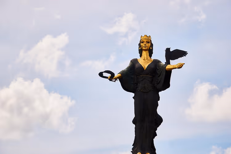 Statue der Heiligen Sofia in Sofia, schwarze Figur mit vergoldetem Gesicht und Krone, mit Kranz und Eule, vor bewölktem Himmel