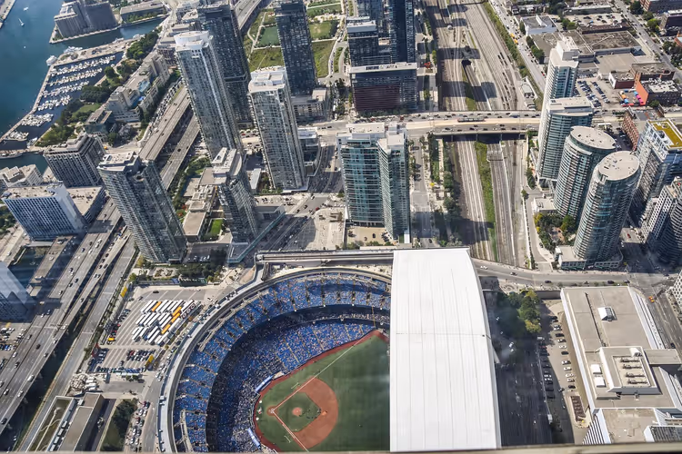 Blick von oben auf Wohntürme in Toronto, Bahngleise und ein Stadion mit geöffnetem Dach und Baseballfeld
