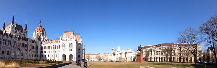 Ungarisches Parlamentsgebäude und ein offener Platz mit Rasen und Reiterstandbild in Budapest unter klarem blauem Himmel