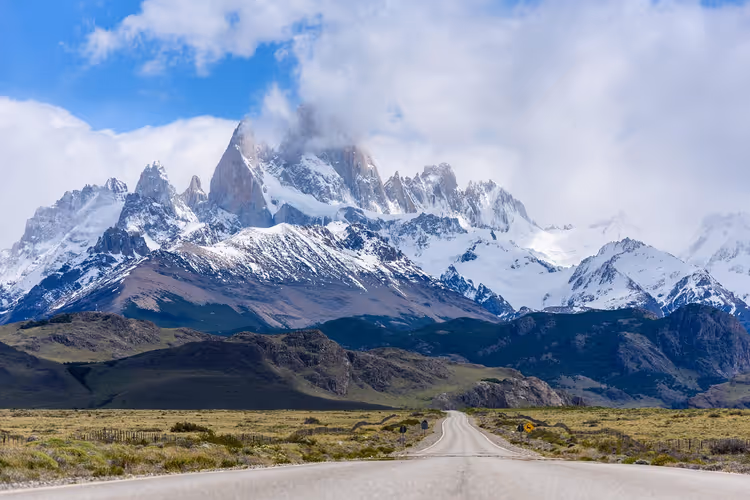 Leere Straße durch die patagonische Steppe in Richtung des schneebedeckten, in Wolken gehüllten Fitz-Roy-Massivs