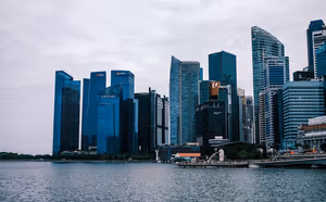 Gläserne Wolkenkratzer des Finanzviertels von Singapur jenseits der Marina Bay unter bedecktem Himmel, am Ufer der Merlion