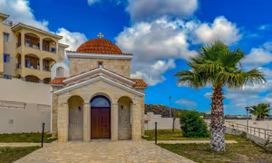 Steinkapelle mit terrakottafarbener Kuppel und Bogenvorhalle neben einer Palme unter bewölktem blauem Himmel in Paphos