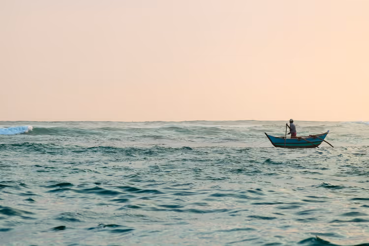 Visser in een boot tegen de zee en zonsondergang