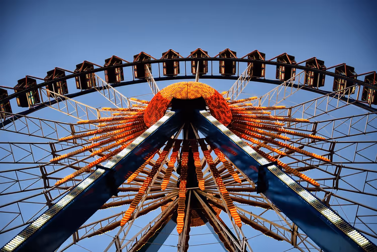 Riesenrad von unten gesehen, Nabe und Speichen mit orangefarbenen Glühbirnen beleuchtet vor tiefblauem Abendhimmel