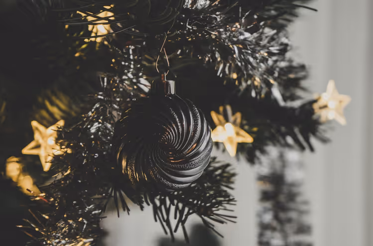 Dunkle gerippte Christbaumkugel an einem Tannenzweig mit Lametta und leuchtenden sternförmigen Lichtern