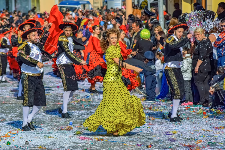 Tänzerin im gelben Kleid mit Punkten und Männer in Matadorkostümen ziehen beim Karneval durch eine mit Konfetti bedeckte Straße