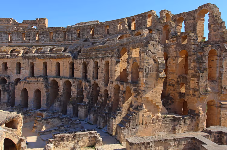 Antikes römisches Amphitheater mit Rängen aus verwitterten Sandsteinbögen unter klarem blauem Himmel in Tunesien