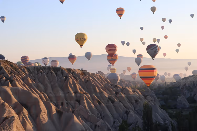 Dutzende bunte Heißluftballons schweben bei Sonnenaufgang über den zerfurchten Felsformationen Kappadokiens
