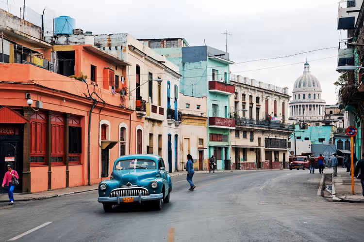 Türkisfarbener Oldtimer auf einer Straße in Havanna mit verblassten pastellfarbenen Häusern, im Hintergrund die Kuppel des Kapitols