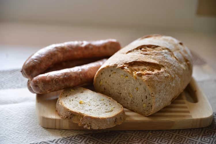 Aufgeschnittener Laib Bauernbrot und geräucherte Würste auf einem Holzschneidebrett, typisch polnische Kost