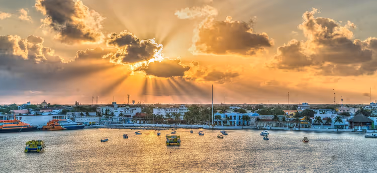 غروب الشمس على واجهة كوزوميل البحرية مع قوارب وأشعة الشمس
