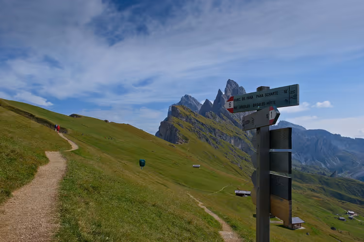 Vägvisare för vandringsled på en grässluttning i Val Gardena med Dolomiternas taggiga toppar i bakgrunden på sommaren