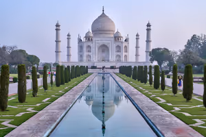 Taj Mahal in Indien spiegelt sich in einem langen, von Zypressen gesäumten Wasserbecken unter dunstigem Morgenhimmel